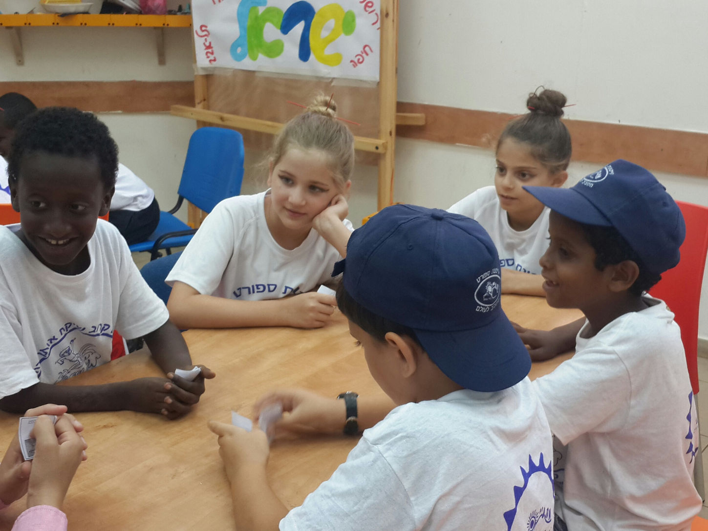 קבוצת ילדים צעירים יושבים סביב שולחן ומשחקים 