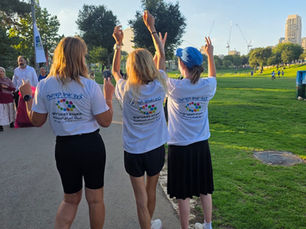Three women stand with their backs to the camera, their hands raised