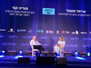 אריאל משעל יושב על כיסא והמראיינת יושבת מול על הבמה 